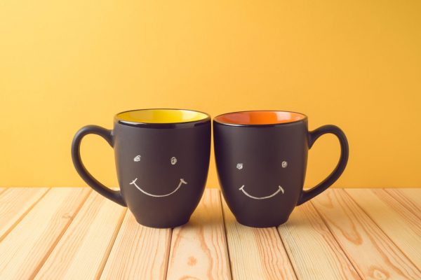 Chalkboard coffee mugs on wooden table with funny cute faces. Friendship day concept