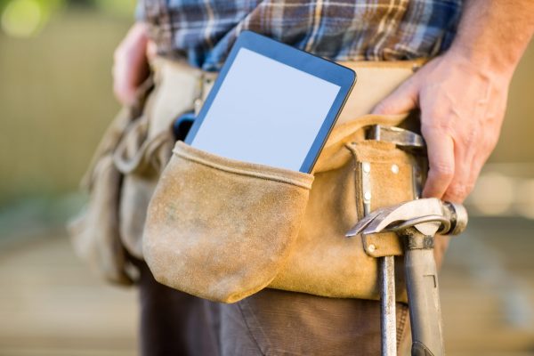 Closeup of digital tablet and hammer in carpenter's tool belt outdoors