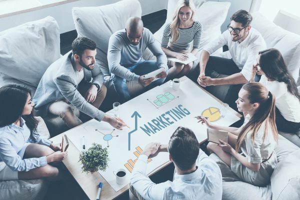 Discussing strategy together. Top view of business people discussing something while sitting around the desk together and pointing large paper with graphs and charts