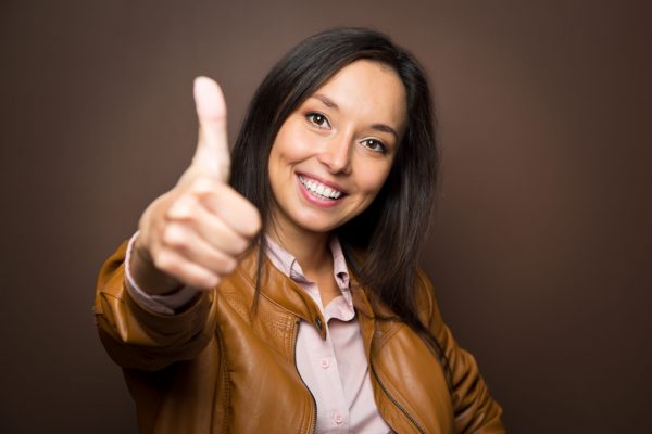 Woman giving thumbs up approval hand sign gesture smiling happy isolated on white background in full body length in high angle perspective view. Content smile on multiracial asian caucasian woman.